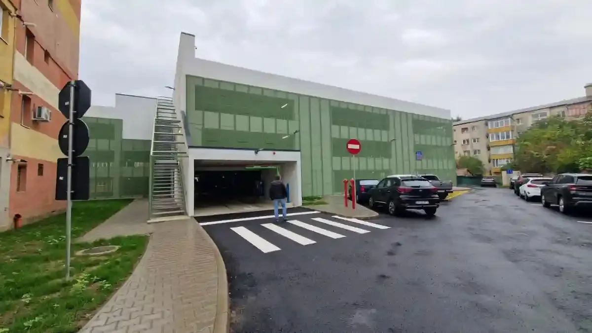 O clădire verde cu intrare pentru vehicule și scară exterioară se află lângă o trecere de pietoni și mai multe mașini.