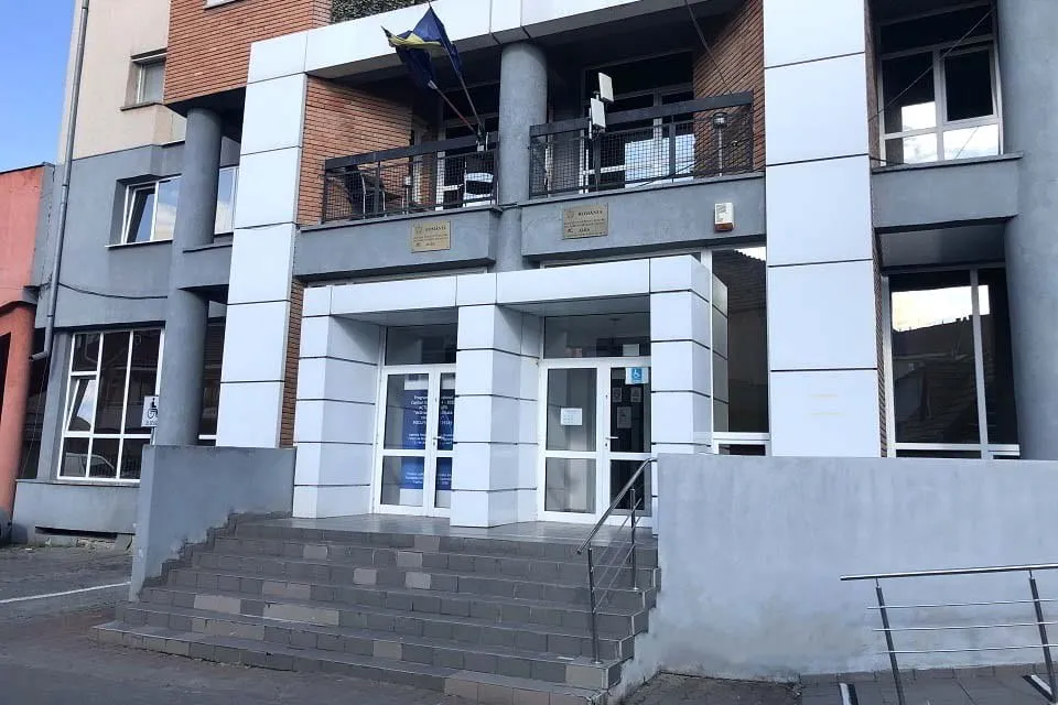 Fațada unei clădiri cu trepte, două intrări vitrate, coloane, ferestre și balustrade metalice.