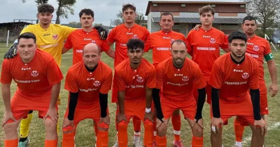 Un grup de fotbaliști în echipamente roșii și galbene pozează pe un teren cu iarbă; cei din față stau aplecați.
