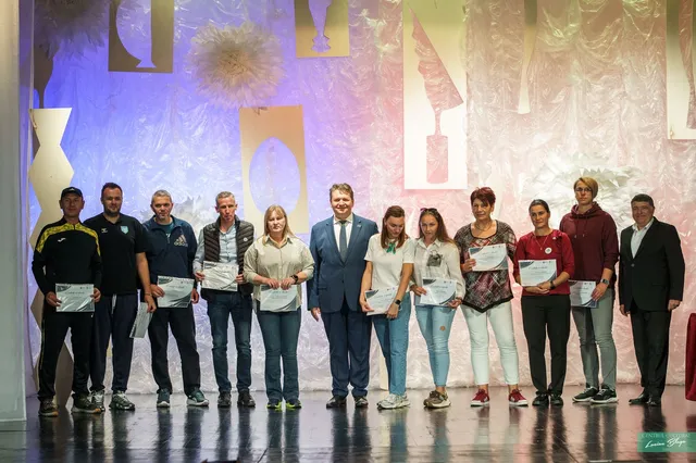 Un grup de adulți și tineri stă pe o scenă, iar mai multe persoane țin diplome în mâini.