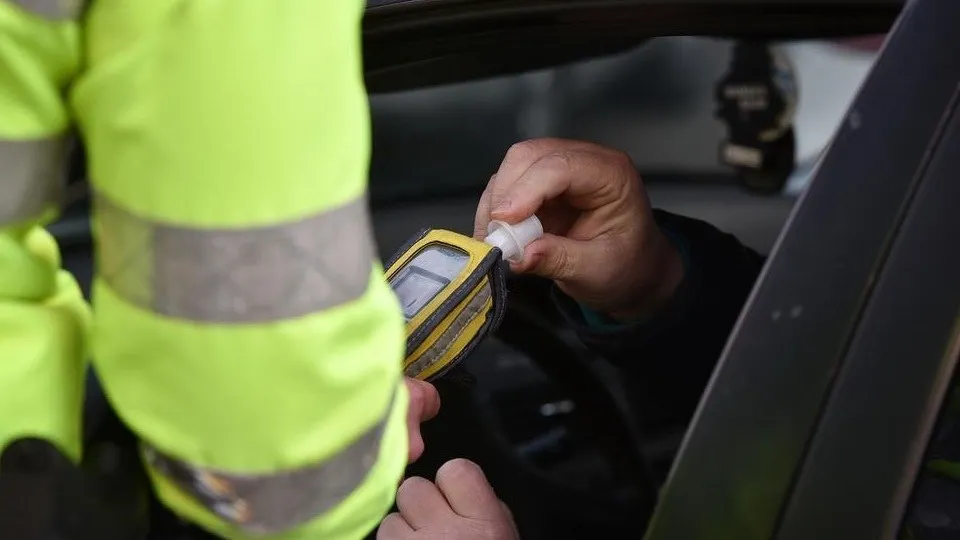 O persoană în vestă fluorescentă ține un dispozitiv lângă mâna unui bărbat aflat într-un autoturism.