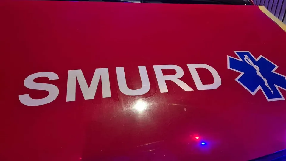 O suprafață roșie prezintă inscripția albă „SMURD”, simbolul medical albastru și reflexii de lumini roșii și albastre.