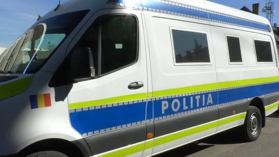 O autospecială albă, cu dungi albastre și verzi, geamuri laterale și inscripția „POLIȚIA”, este fotografiată din lateral.