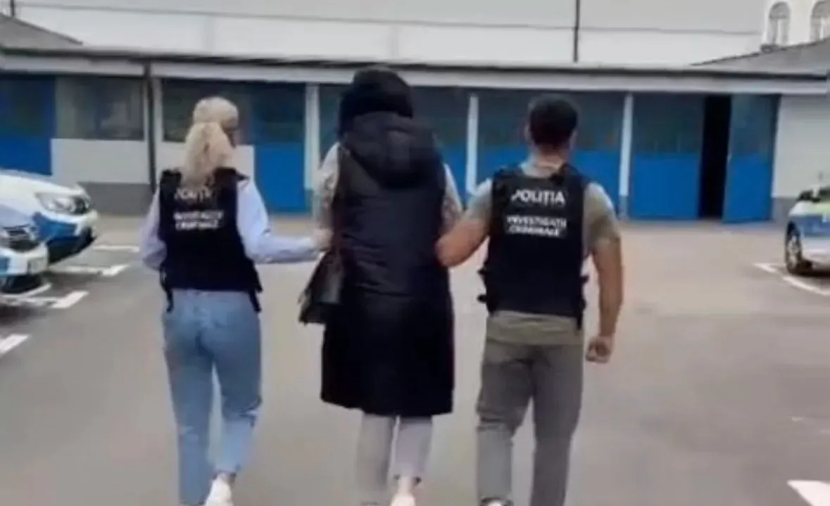 Trei persoane văzute din spate merg pe o alee; cele de la margini poartă veste negre cu inscripții albe.