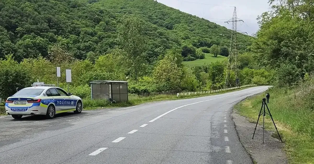 O autospecială albă cu marcaje albastre este oprită lângă un drum, iar un dispozitiv pe trepied stă pe marginea opusă.