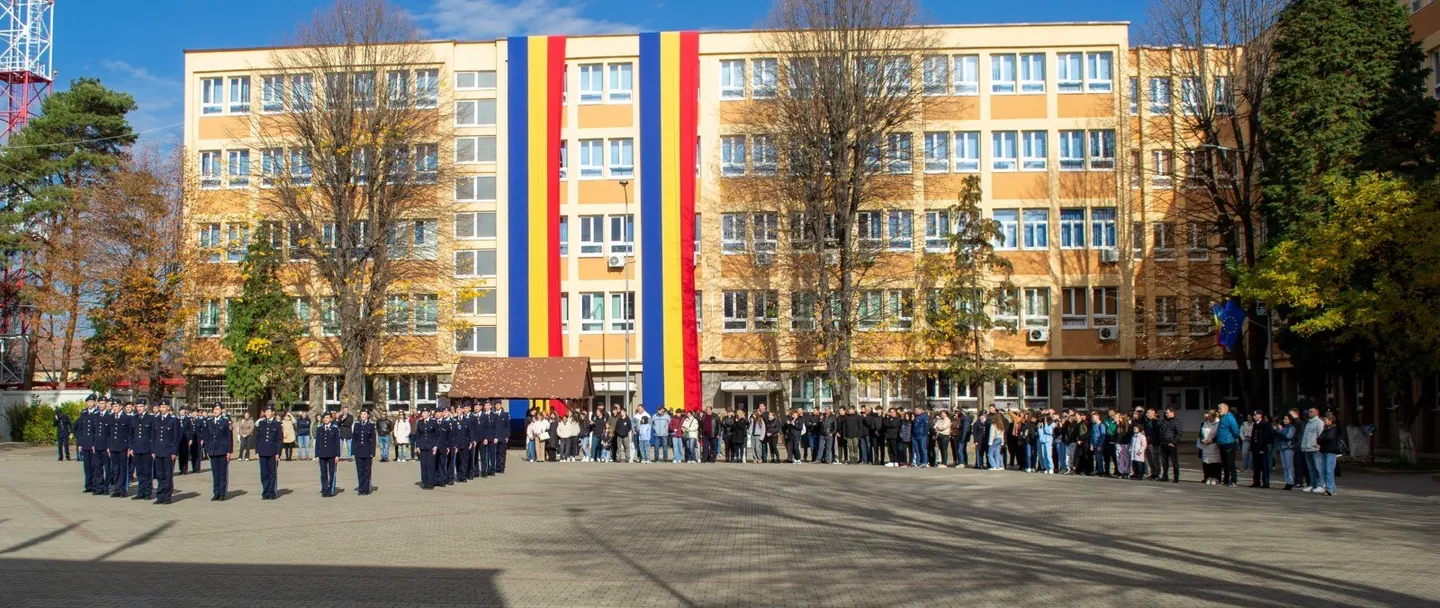 În fața unei clădiri cu multe ferestre și benzi verticale colorate, mai multe grupuri de persoane stau pe o alee largă.