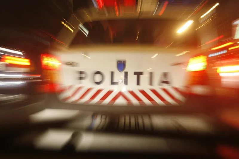 Partea din spate a unui vehicul de poliție este fotografiată noaptea; se văd inscripția „POLIȚIA”, dungi roșii și lumini aprinse.