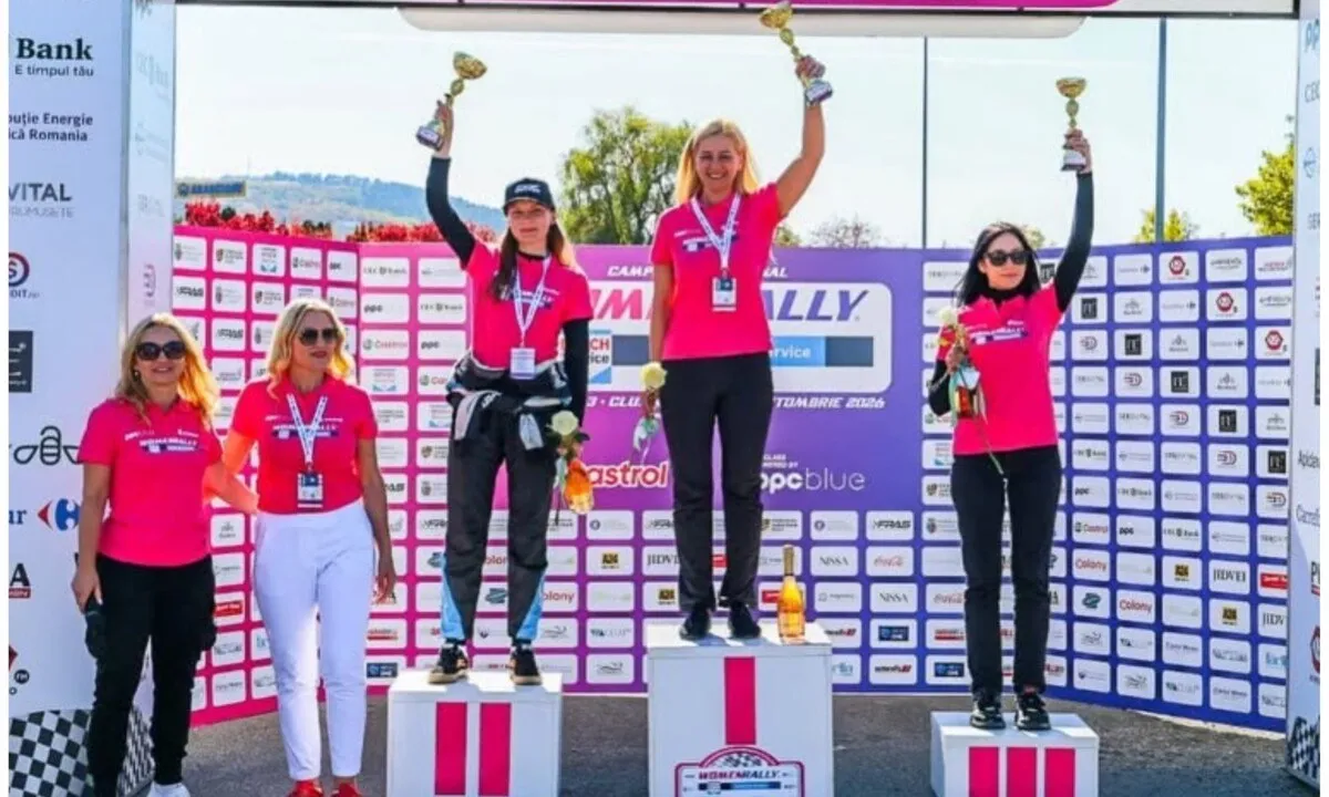 Trei femei cu tricouri roz stau pe podium, ridicând trofee, iar alte două femei se află în fața panoului cu sponsori.