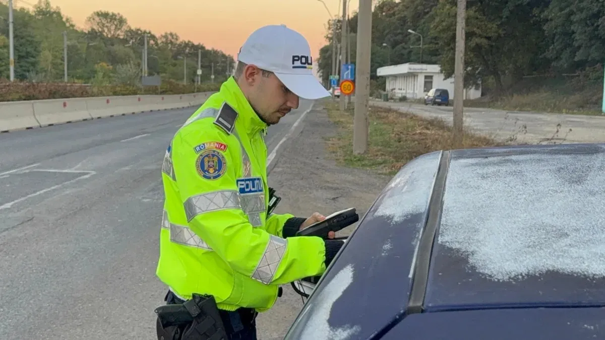 Un polițist în uniformă reflectorizantă ține un dispozitiv lângă portiera unui autoturism oprit pe marginea unui drum.