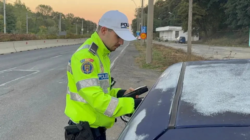 Un polițist în uniformă reflectorizantă ține un dispozitiv lângă portiera unui autoturism oprit pe marginea unui drum.