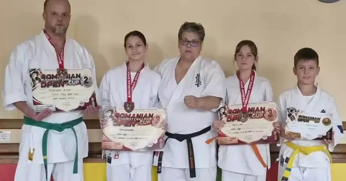 Cinci persoane în uniforme albe de arte marțiale stau aliniate; mai multe poartă medalii și țin diplome în față.