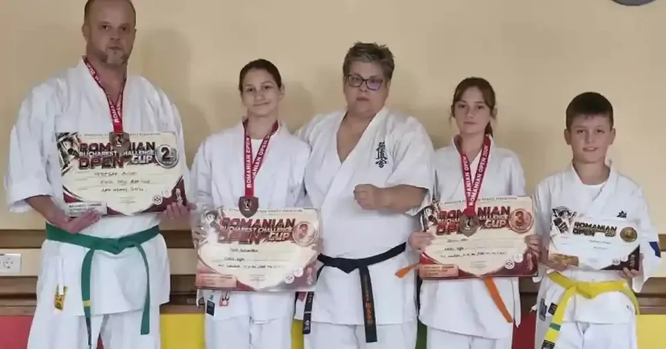 Cinci persoane în uniforme albe de arte marțiale stau aliniate; mai multe poartă medalii și țin diplome în față.