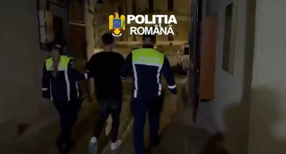 Doi bărbați în veste reflectorizante însoțesc un bărbat îmbrăcat în negru pe un coridor slab luminat.