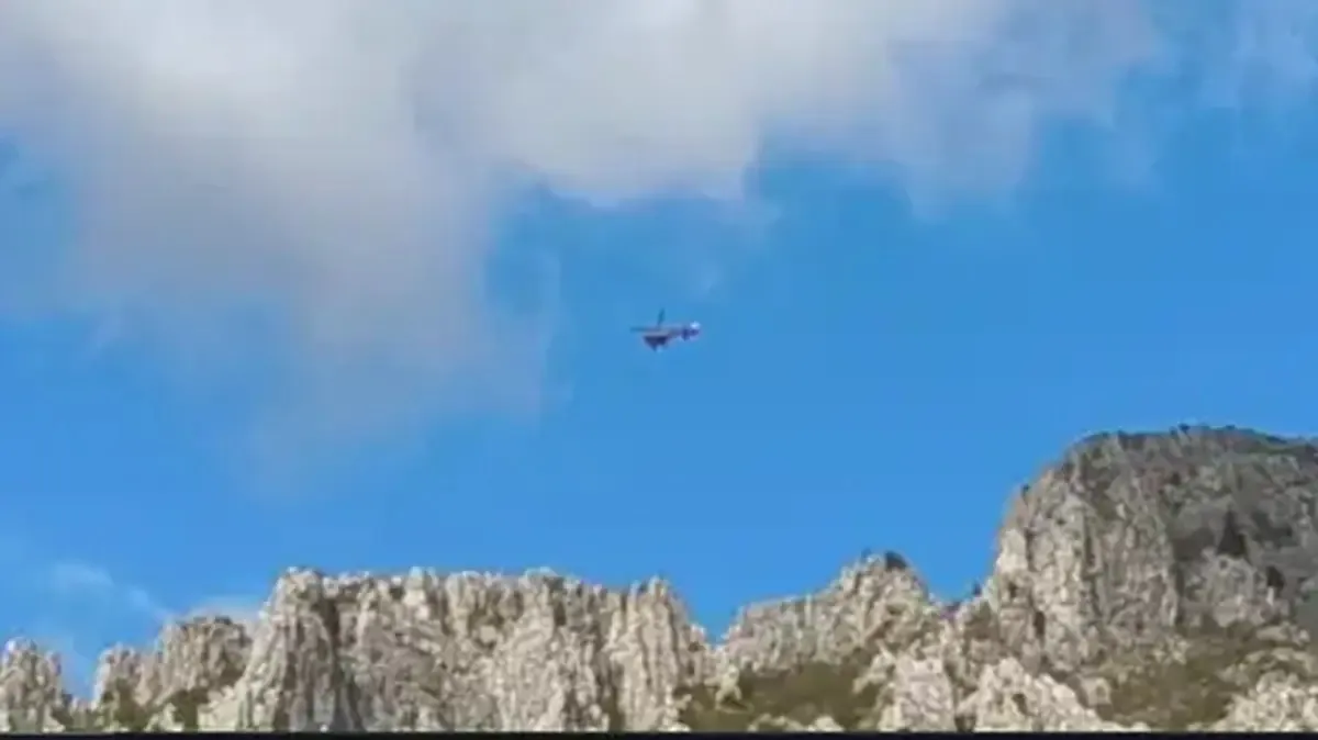 Un elicopter mic zboară pe un cer albastru deasupra unor stânci deschise la culoare.