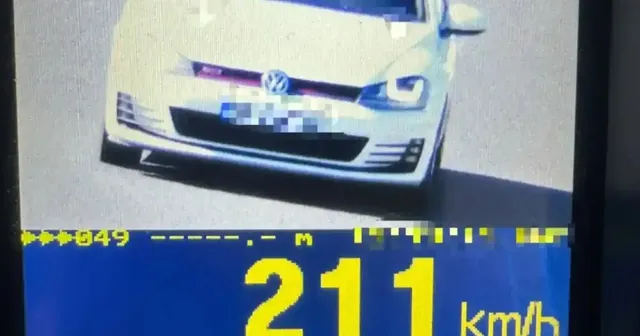 Un autoturism alb apare pe un ecran, deasupra valorii galbene „211 km/h”, iar plăcuța de înmatriculare este pixelată.