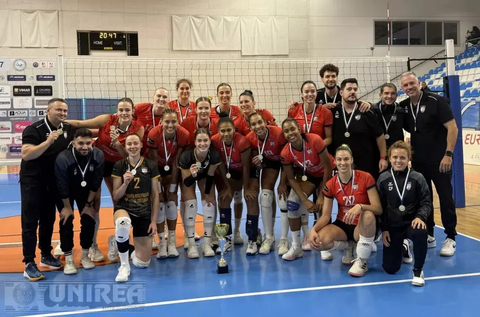 Un grup de persoane în echipament sportiv pozează pe un teren albastru, în fața unui fileu; se văd medalii și un trofeu.