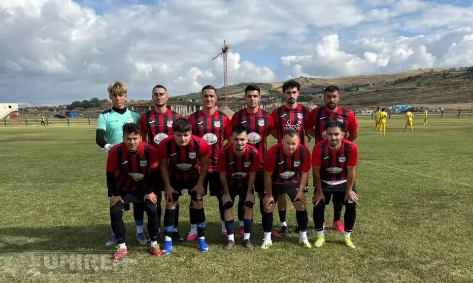 Unsprezece fotbaliști în echipamente roșii și negre pozează pe un teren, iar jucători în galben se află în fundal.