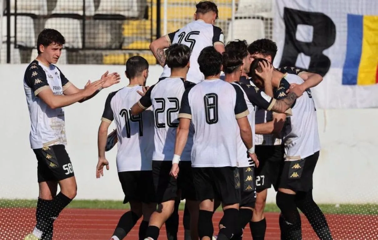 Mai mulți fotbaliști în tricouri alb-negre se strâng lângă marginea terenului; pe spatele a trei tricouri se văd numerele 15, 22 și 8.
