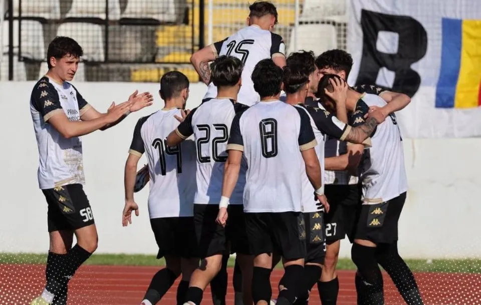 Mai mulți fotbaliști în tricouri alb-negre se strâng lângă marginea terenului; pe spatele a trei tricouri se văd numerele 15, 22 și 8.